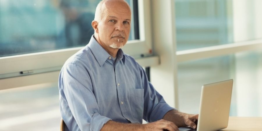 Astute senior businessman giving the camera an assessing thoughtful look as he sits working at a laptop computer in a spacious modern office
