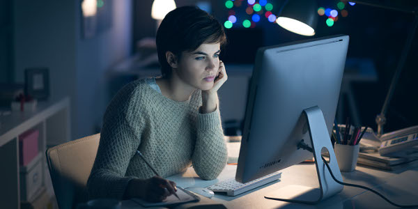 Young woman working and studying late at night, she is connecting with her computer and writing down notes on a notepad