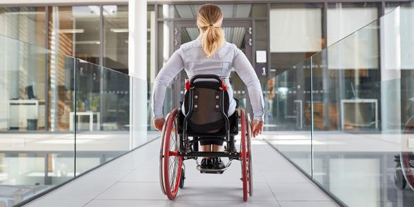 Gelahmte Frau im Rollstuhl unterwegs im behindertengerechten Burohaus