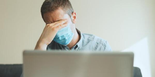 Tired man in medical mask working on the computer indoors.